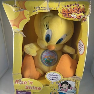 May include: Yellow Tweety Bird plush alarm clock toy in a yellow box with the words "Tweety Alarm Clock" and "Rise'n Shine" on it. The clock face is visible on the toy's chest. The box has a picture of Tweety Bird waking up a girl in bed.