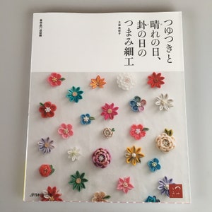 May include: A book cover with the title "Tsumiki to Hare no Hi,  Mainichi no  Tsumami Zaiku" in Japanese. The cover features a variety of colorful fabric flowers.