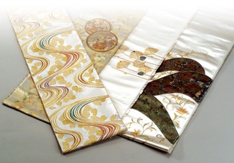 Pu&ograve; includere: Un set di tre pannelli in tessuto di seta bianca con disegni dorati e marroni. I pannelli presentano una variet&agrave; di motivi, tra cui linee a spirale, foglie e forme geometriche.