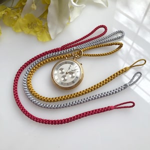 Peut inclure: Trois chaînes de montre en rouge, or et argent. Les chaînes sont tressées et ont une boucle à chaque extrémité. Une montre de poche en or est suspendue aux chaînes.
