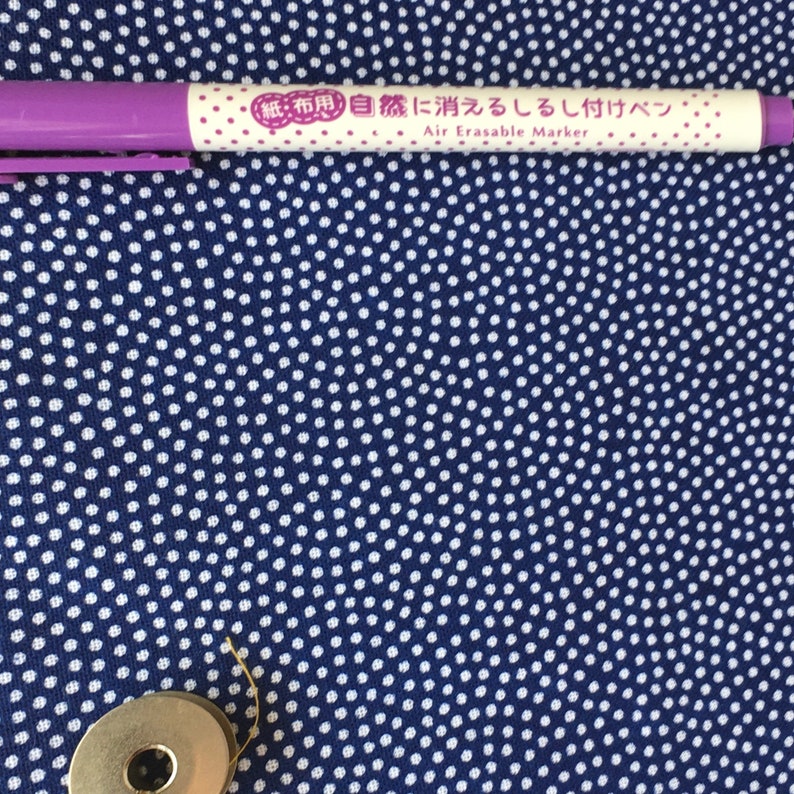 May include: A purple fabric marker with white polka dots and the text "Air Erasable Marker" in Japanese and English. The marker is on a blue fabric with white polka dots.