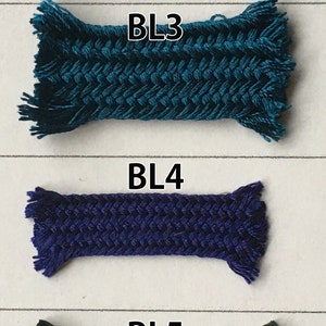 May include: Close-up of six samples of braided cord in various shades of blue, teal, purple, green, and black. Each sample is labeled with a "BL" followed by a number. The cords are tightly woven with a textured appearance.
