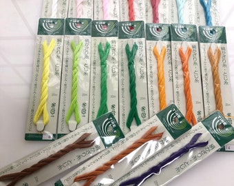 May include: Assortment of colorful braided cords, each packaged individually with a green label that reads "TIRE" and includes the text "絹かざり糸・とじ糸" in Japanese. The cords are 20 meters long and are labeled with the text "パッチワークキルトの飾り縫いや、ふとん・座ぶとん・クッション類のかざりとじに" in Japanese.