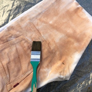 May include: A white fabric with a brown stain and a green paintbrush with a wooden handle.