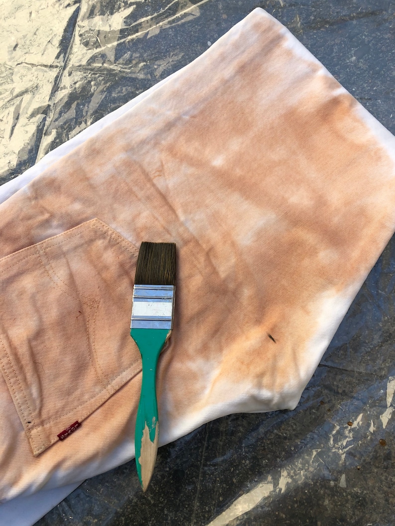 May include: A white fabric with a brown stain and a green paintbrush with a wooden handle.