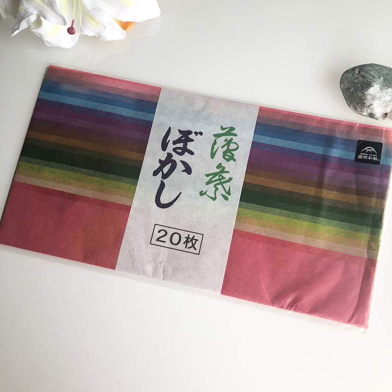 May include: A package of 20 sheets of colorful Japanese washi paper. The paper is arranged in a rainbow pattern and has a label with Japanese text that reads "Washi Paper" and "20 sheets".