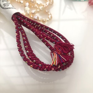 May include: A set of four burgundy cords with colorful threads woven into the fabric. The cords have tassels at the ends.