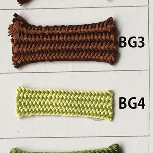 May include: A color chart featuring six samples of braided cord in various shades. The colors range from light brown to dark green. Each sample is labeled with a "BG" followed by a number, indicating different color variations.