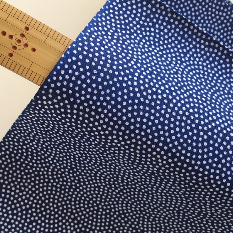 May include: A close-up of a blue fabric with a white polka dot pattern. The fabric has a subtle wave-like texture.