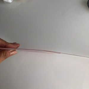 May include: A clear plastic sheet with a slight pink tint. The sheet is being held up by a hand.