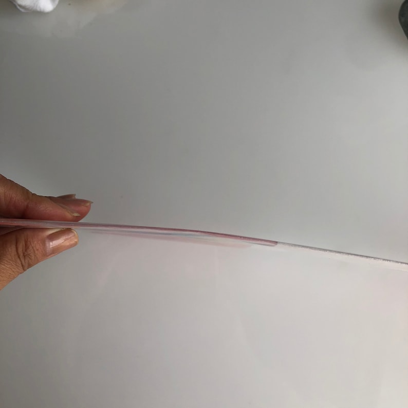 May include: A clear plastic sheet with a slight pink tint. The sheet is being held up by a hand.