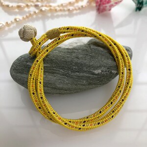 May include: A yellow rope bracelet with a knot at the end. The rope is woven with orange and black threads.