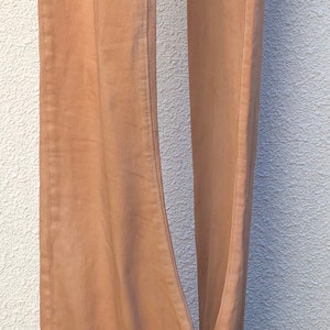 May include: A pair of light brown pants hanging on a clothes rack. The pants are made of a soft, woven fabric and have a relaxed fit.