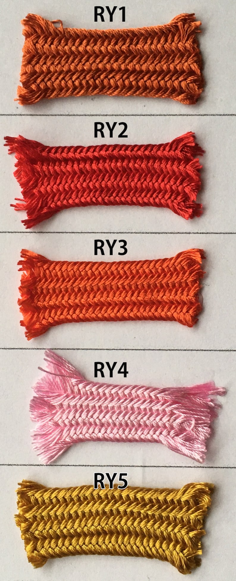 May include: Five samples of braided cord in various colors: orange, red, light orange, pink, and gold. Each sample is rectangular with a herringbone pattern and frayed ends. The samples are labeled RY1 through RY5.