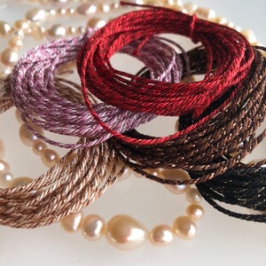 May include: A close-up of a collection of colorful embroidery floss spools. The spools are arranged in a circular pattern and are made of different colors, including red, brown, pink, and gold.