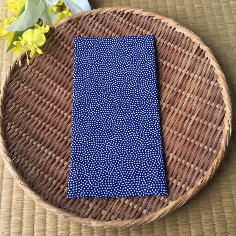 May include: A blue fabric napkin with a white polka dot pattern. The napkin is lying on a woven basket.