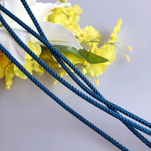 May include: Three strands of teal blue cord or rope, lying on a white surface with yellow flowers.