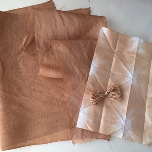May include: Two pieces of fabric dyed in shades of brown. One piece is folded and the other is flat. A piece of twine is on top of the fabric.