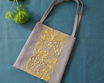 May include: A gray linen tote bag with a floral design embroidered in yellow thread. The bag has two straps.