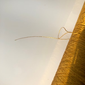 May include: A spool of gold metallic thread with a strand extending outward. The thread is a bright, shimmering gold color. The spool is partially visible, showing the tightly wound thread. This image is suitable for craft and sewing projects.