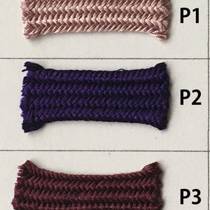 May include: Three samples of braided cord in different colors. The top cord is a light pink, the middle is a deep purple, and the bottom is a dark burgundy. Each cord has a textured, woven pattern and is labeled with a "P" followed by a number.