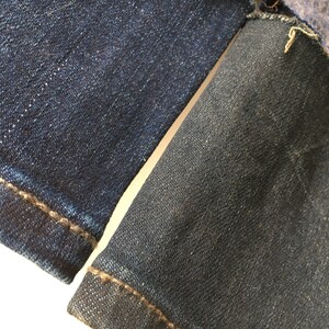 May include: Close-up of two pieces of dark blue denim fabric sewn together. The fabric has a textured weave and a subtle sheen.