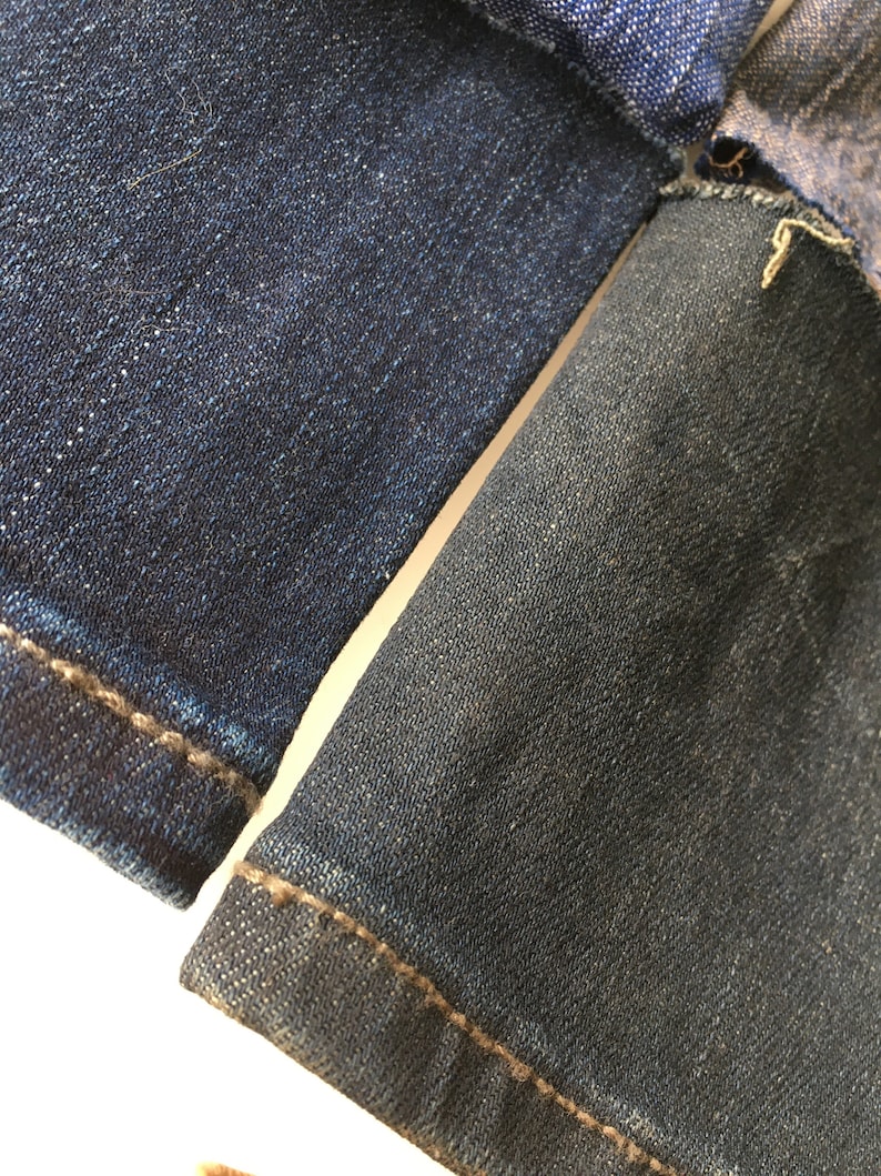 May include: Close-up of two pieces of dark blue denim fabric sewn together. The fabric has a textured weave and a subtle sheen.