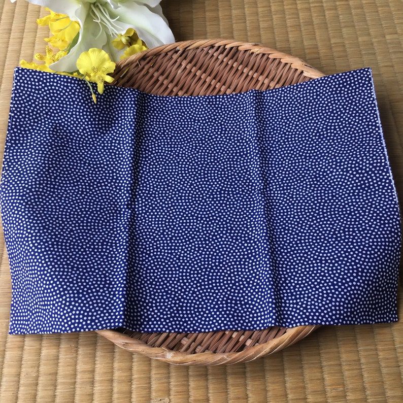 May include: A folded blue fabric with a white polka dot pattern. The fabric is folded in thirds and is lying on a woven basket.