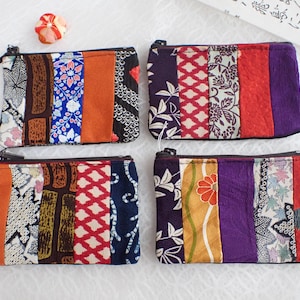 May include: Four colorful fabric coin purses with zipper closures. Each purse is made of different patterned fabrics in shades of red, orange, blue, green, purple, and white.