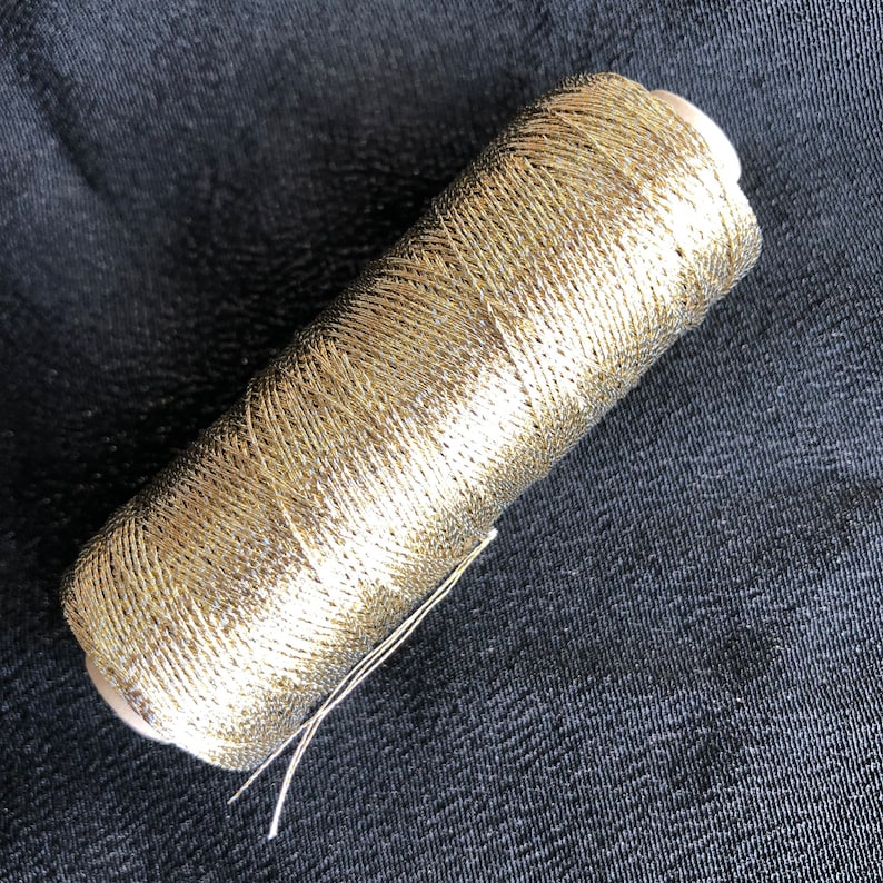 Pu&ograve; includere: Un'bobina di filo metallico dorato. Il filo &egrave; avvolto strettamente attorno alla bobina e ha una finitura lucida e metallica.