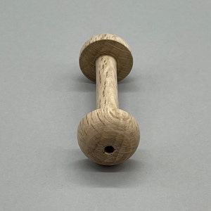 Peut inclure: Une bobine en bois avec un trou au centre. La bobine est en bois brun clair et a une surface lisse et arrondie.