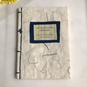 Könnte beinhalten: Ein Buch mit dem Titel "Awa No Kusazome: Namida Iro" mit einem blauen Einband und weißem Text. Der Untertitel lautet "The Dye Plants of Awa; the color of tears".