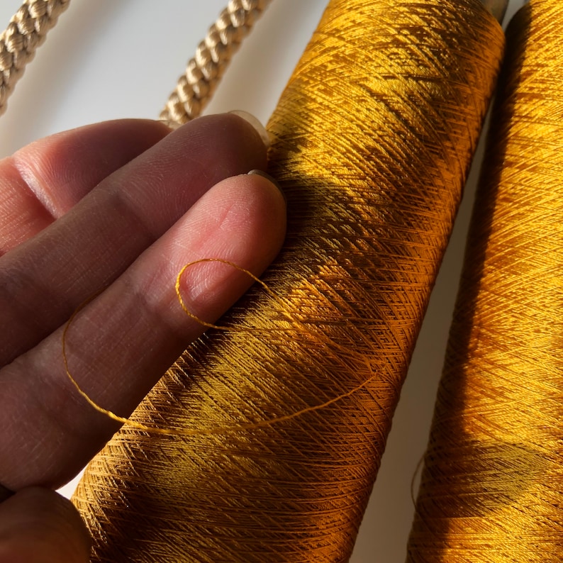 May include: Close-up of golden-yellow spools of thread, with a strand of thread pulled away. The thread is a vibrant, metallic color, and the spools are tightly wound. A gold-colored rope is visible in the background.