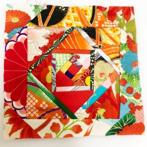 May include: A colourful patchwork quilt block with a geometric design. The block is made of various fabrics with floral patterns in shades of red, orange, yellow, green, blue, and white.