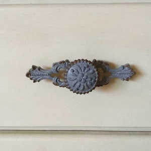 May include: A silver drawer pull with a decorative floral design. The pull has a rounded knob and a long, curved handle.