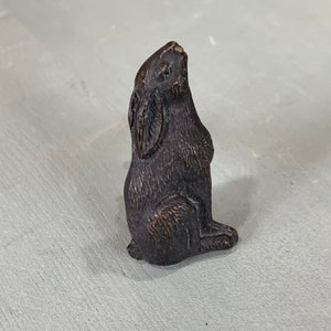 May include: A small, dark brown rabbit figurine with a textured surface. The rabbit is sitting upright with its ears perked up.
