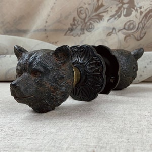 May include: A black bear head door knob with a detailed carved design. The knob is made of metal and has a brass accent.