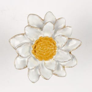 May include: A white ceramic flower with a yellow centre. The flower has a glossy finish and is accented with gold trim.