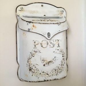 May include: White metal mailbox with a distressed finish and the word "POST" in black lettering. The mailbox has a floral design and a bird silhouette.