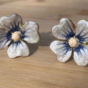 May include: A pair of white and blue enamel flower-shaped drawer pulls with gold accents. The flowers have a five-petal design with a blue centre and white swirls.