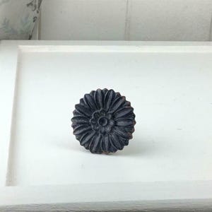 May include: A dark grey, flower-shaped cabinet knob with detailed petal carvings. The knob has a slightly distressed finish, adding a vintage or rustic aesthetic. The hardware is designed for furniture and home decor projects.