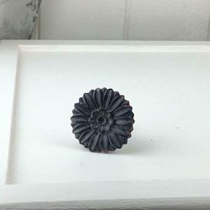 May include: Black metal flower-shaped cabinet knob with a raised design.