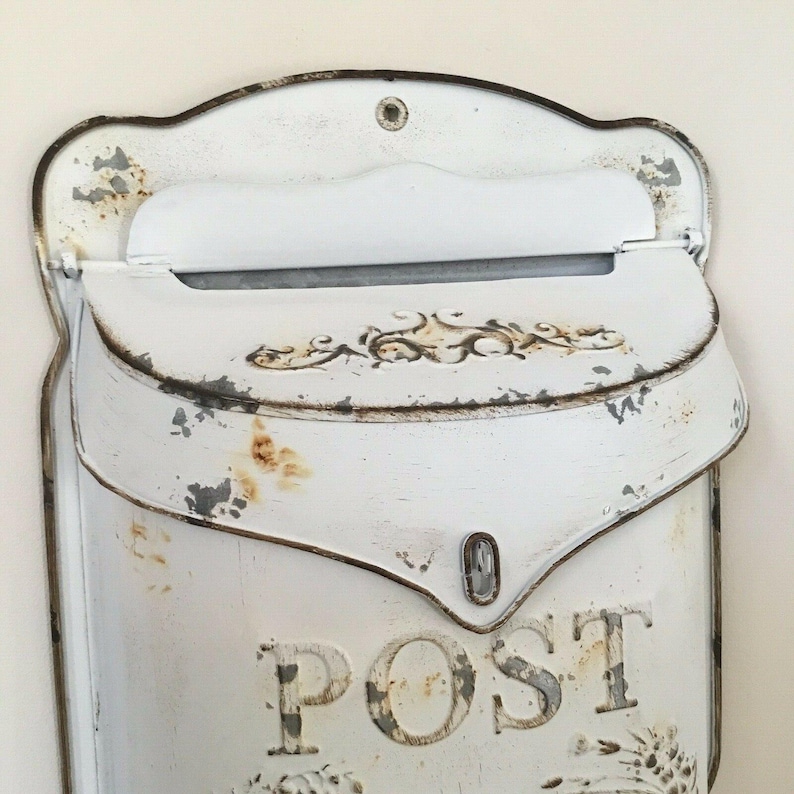 Pu&ograve; includere: Cassetta postale in metallo bianco con finitura usurata e la parola "POST" in rilievo sul davanti. La cassetta postale ha uno sportello che si apre per rivelare una fessura per la posta.