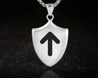 May include: A silver-colored pendant necklace featuring a shield-shaped charm. The charm has a black arrow pointing upwards against a white background. The necklace chain is a linked design.
