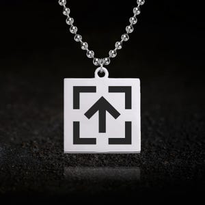 May include: Silver pendant necklace. The square pendant has a black arrow pointing upwards within a square frame. The necklace has a ball chain. The background is dark.