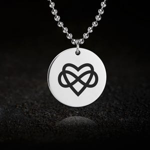 Op de afbeelding: Een zilveren ketting met een ronde hanger met een oneindigheidssymbool dat is verweven met een hart. De hanger zit aan een zilveren ketting.