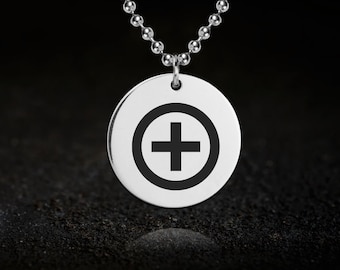 May include: A silver-colored necklace with a round pendant. The pendant features a black plus sign inside a black circle. The necklace has a ball chain design and is displayed against a dark background.