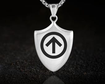 May include: A silver-colored pendant necklace featuring a shield-shaped charm. The charm has a black arrow symbol inside a circle. The necklace chain is a linked design. The background is dark.