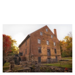 May include: A brick building with a water wheel in front of it. The building has a chimney and several windows. The building is surrounded by trees and grass.