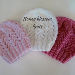 May include: Three knitted hats in pink, white, and red. The hats are made with a lacy stitch pattern. The text "Honey blossom knits" is visible in the image.